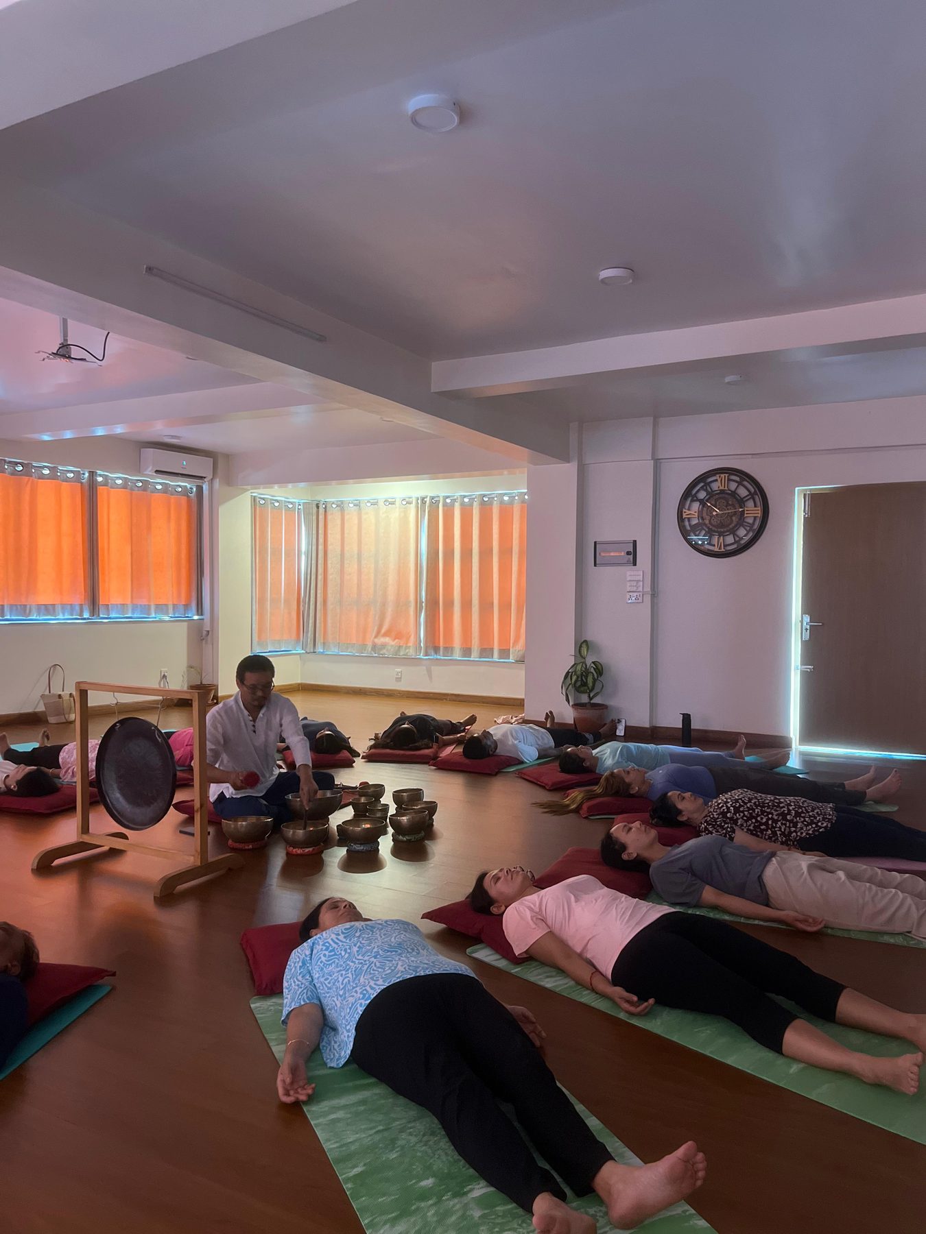 Teacher striking a singing bowl beside a gong while students rest in savasana at a sound bath in Kathmandu, Nepal