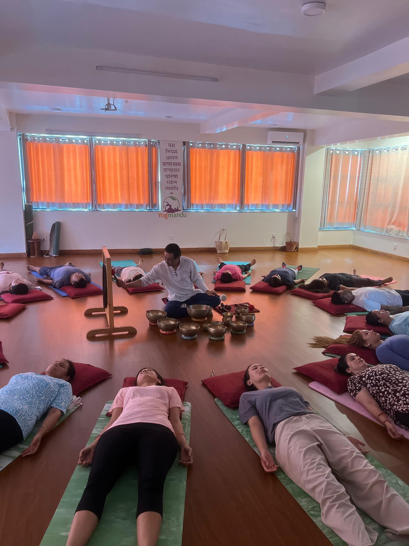 Arjuna seated with a set of Tibetan singing bowls as a large group lies in savasana during a sound healing session at Yogmandu, Kathmandu