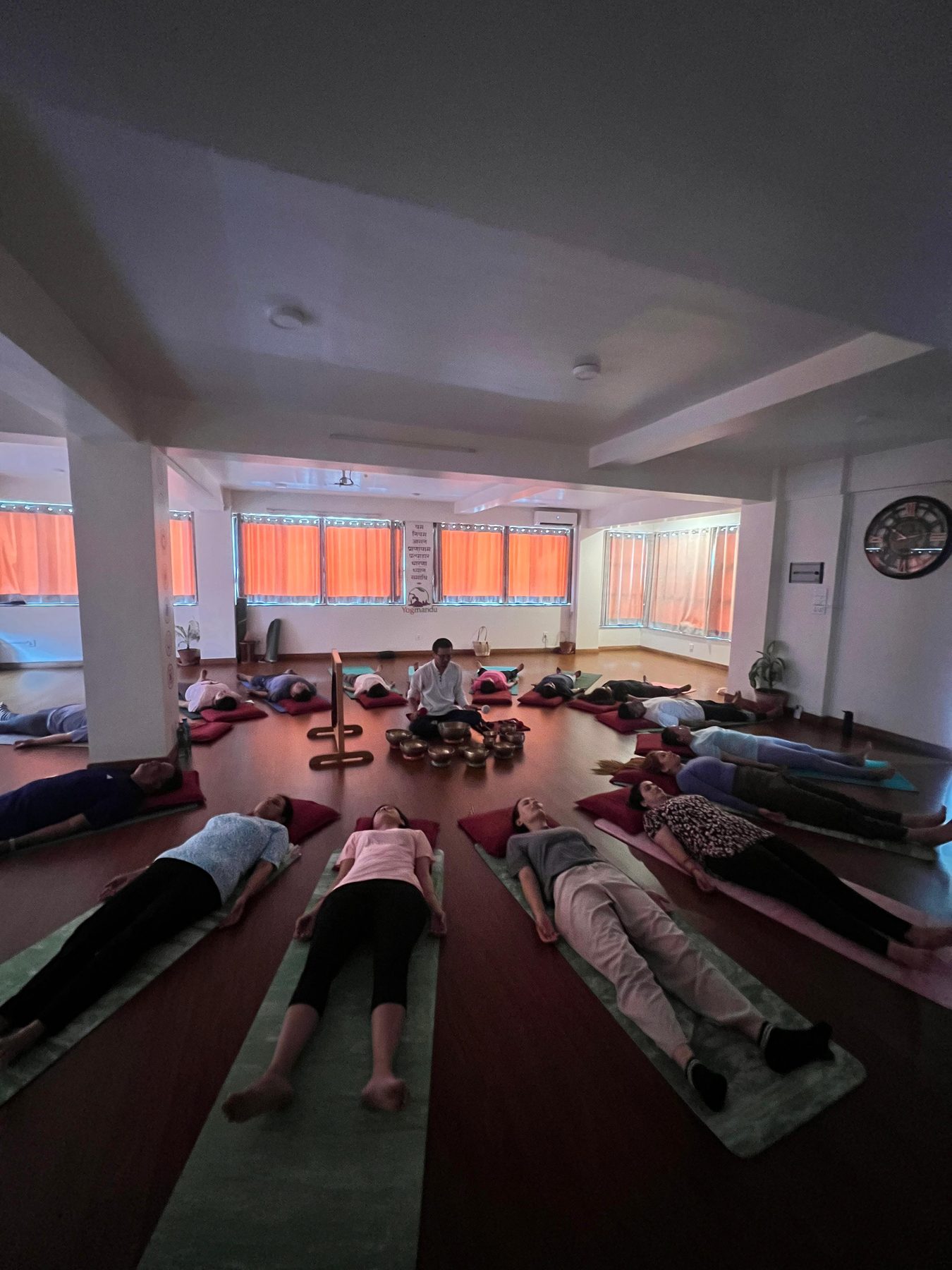 Dimly lit sound healing session at Yogmandu, Kathmandu, with students resting in savasana around the teacher