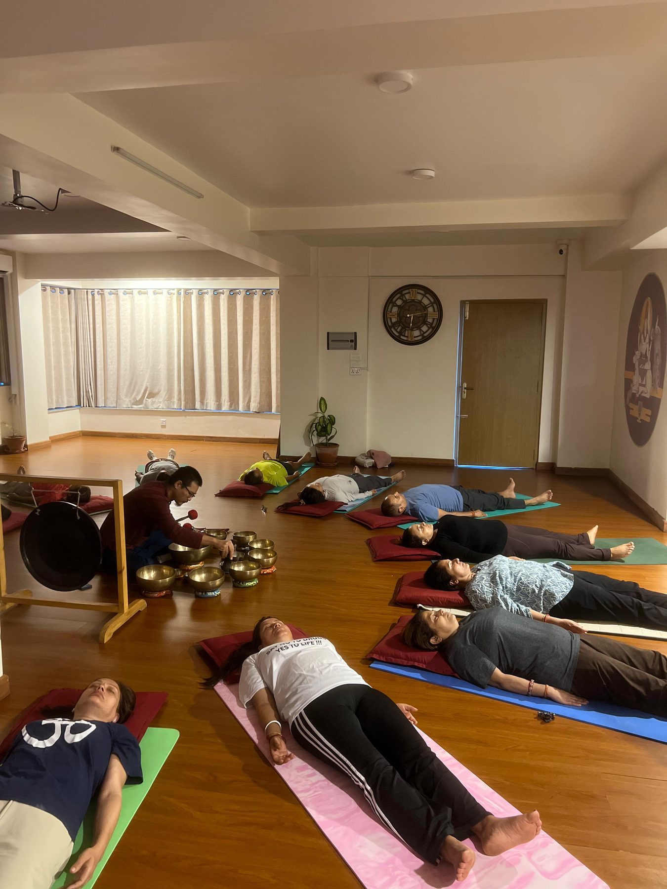 Teacher playing singing bowls and a gong for a group lying in savasana at a sound therapy session in Nepal